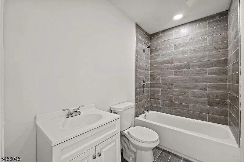Modern renovated bathroom with gray wood-look tile shower surround, white vanity, white toilet, and recessed ceiling light.