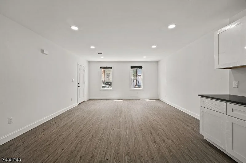 Open kitchen and living area with white cabinetry, black countertops, and wood-look luxury vinyl plank flooring.