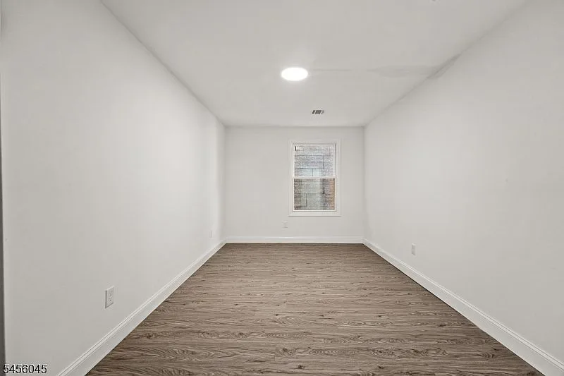 A bright neutral bedroom with light wood-look flooring, white walls, white trim, and a window.