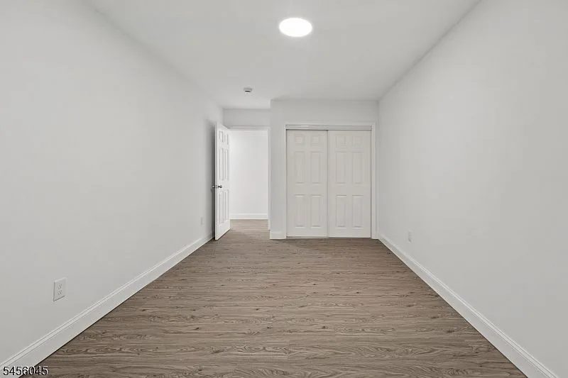 A minimalist bedroom with white walls, wood-look plank flooring, and recessed lighting.