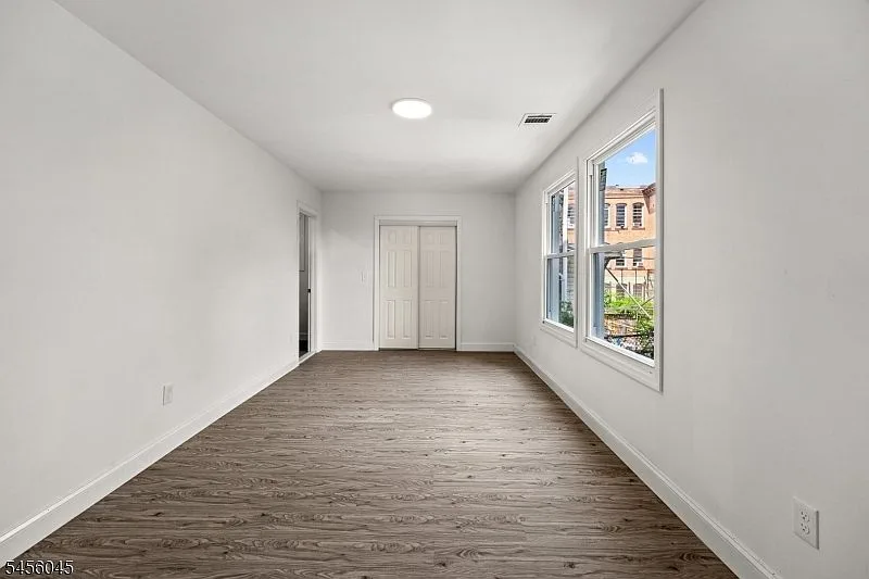 An empty bedroom with gray wood-look laminate flooring, white walls, and white closet doors.