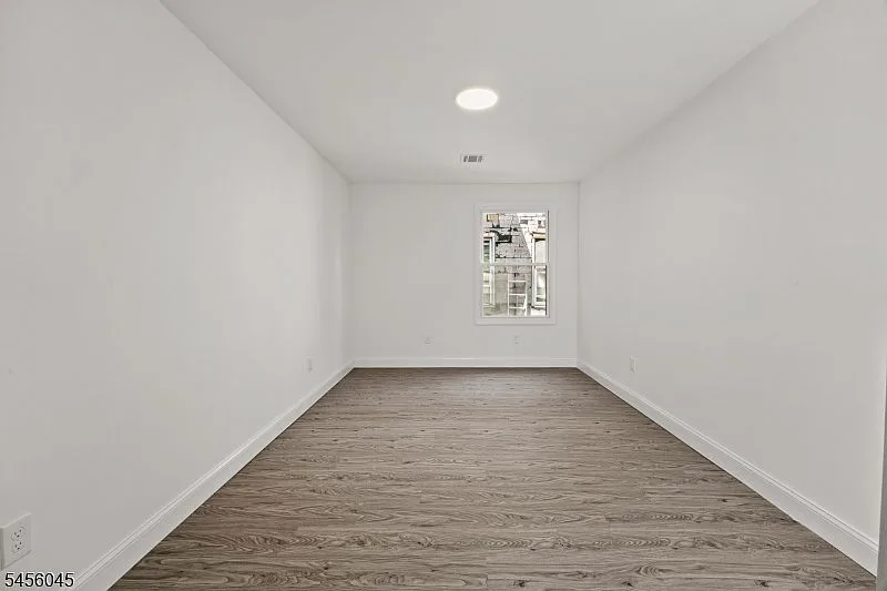 A neutral gray bedroom with a single window, gray wood-look plank flooring, and recessed lighting.