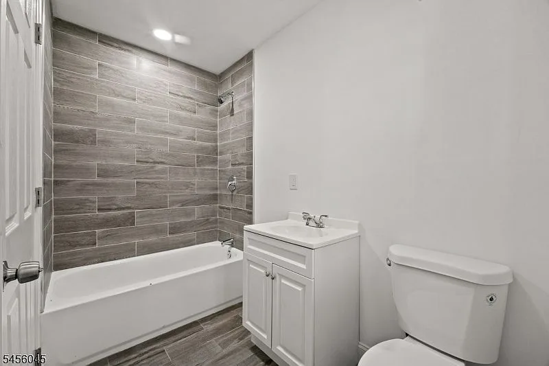 Renovated bathroom with white vanity, gray wood-look tiled tub and shower area, and neutral walls.