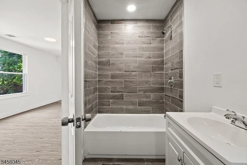 Bathroom seen from the doorway with white vanity, chrome faucet, and gray wood-look tiled shower surround.