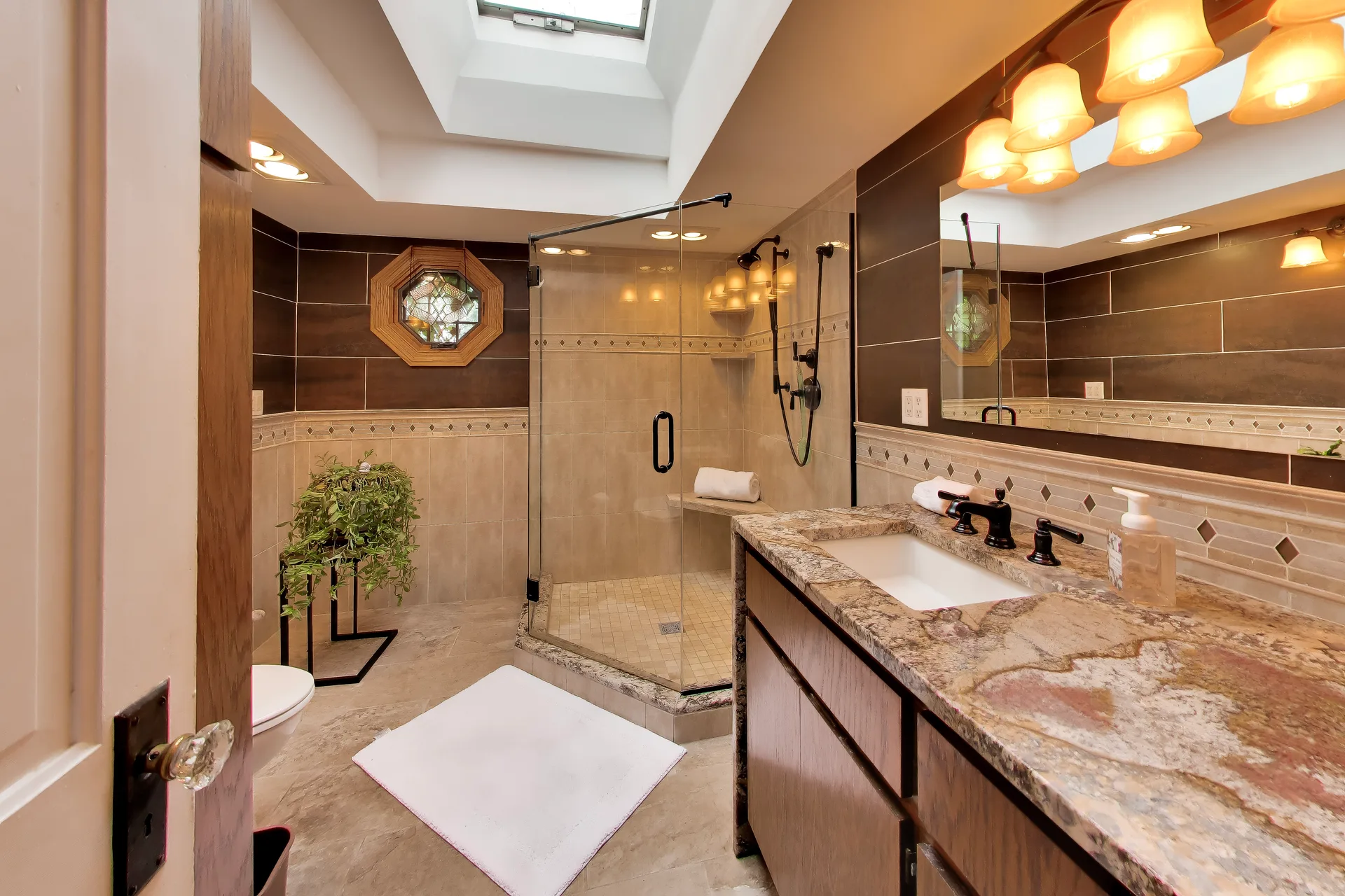 Master bathroom with skylight, wood vanity, and stone counters