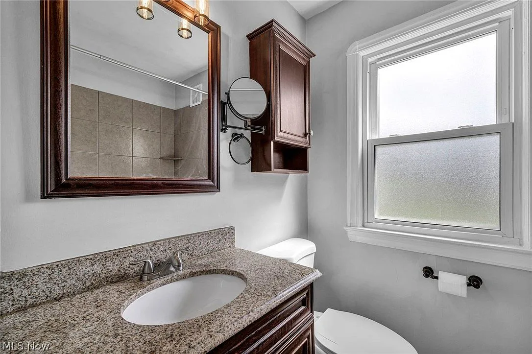 Bathroom vanity with dark wood cabinet, granite countertop, and frosted window