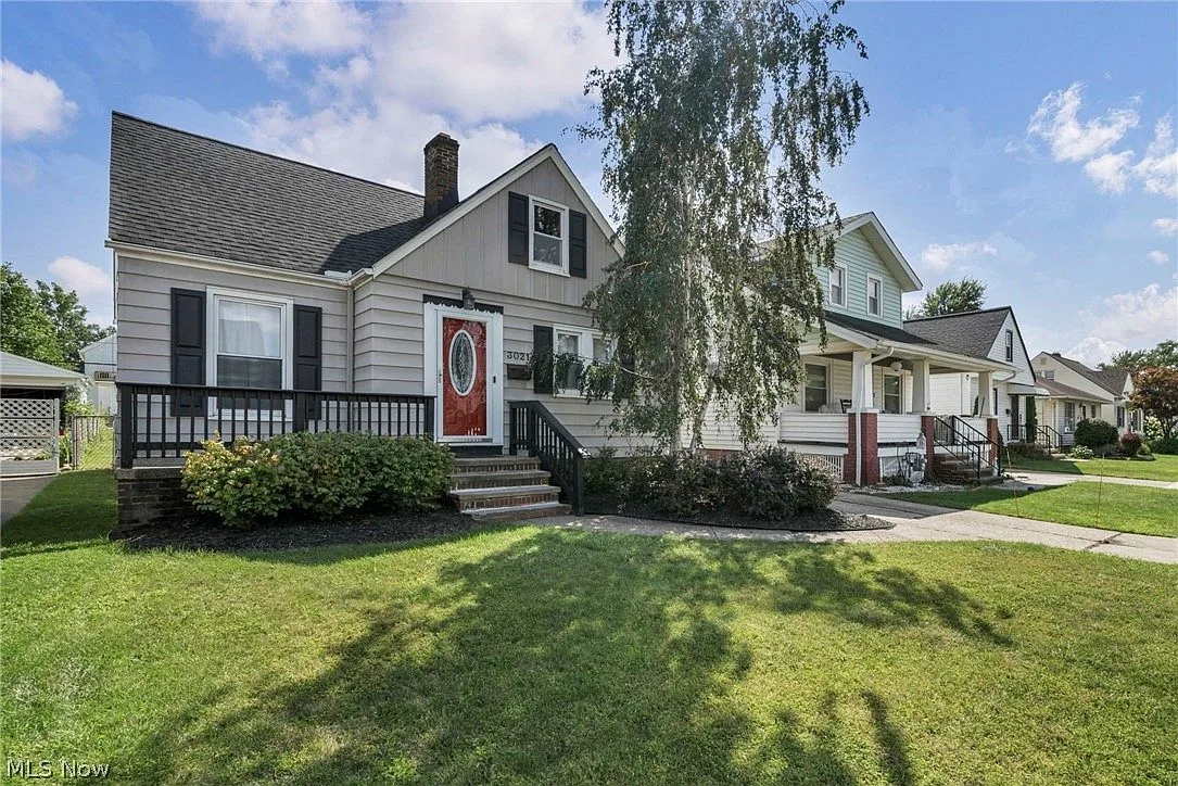 Front facade with red door, black shutters, and a front porch with black railing