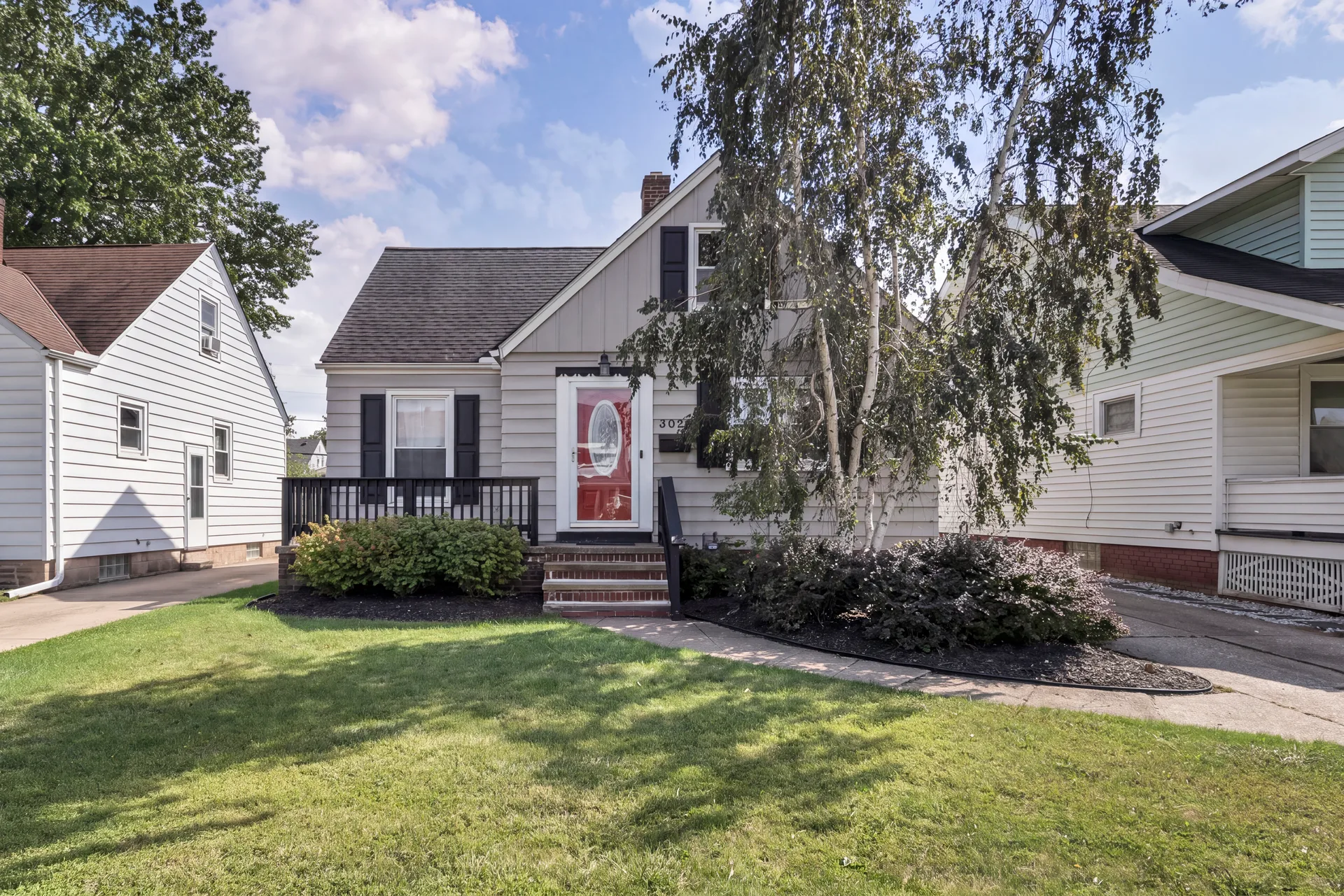 Front of the 3021 Tuxedo Ave bungalow in Parma, Ohio with light grey siding and a red front door