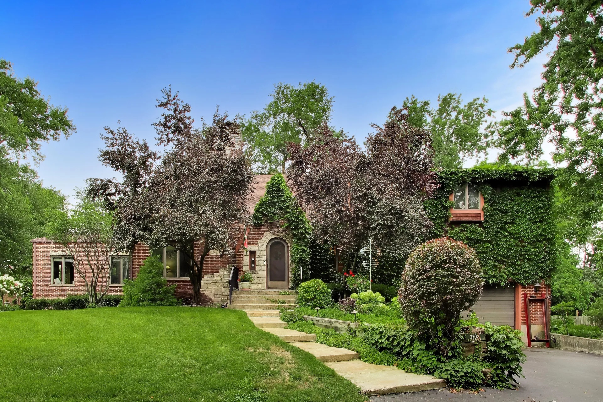 Brick and stone facade of 3708 Cooper Place, a Tudor-style home with an arched entry wrapped in ivy