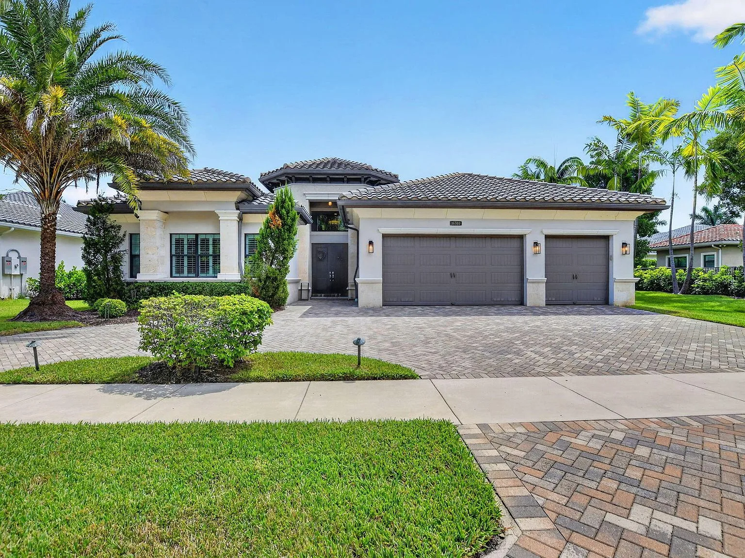 Straight-on view of the single-story lakefront home at 16740 Strasbourg Lane, a modern Mediterranean facade with stone accents and manicured palms in Seven Bridges, Delray Beach