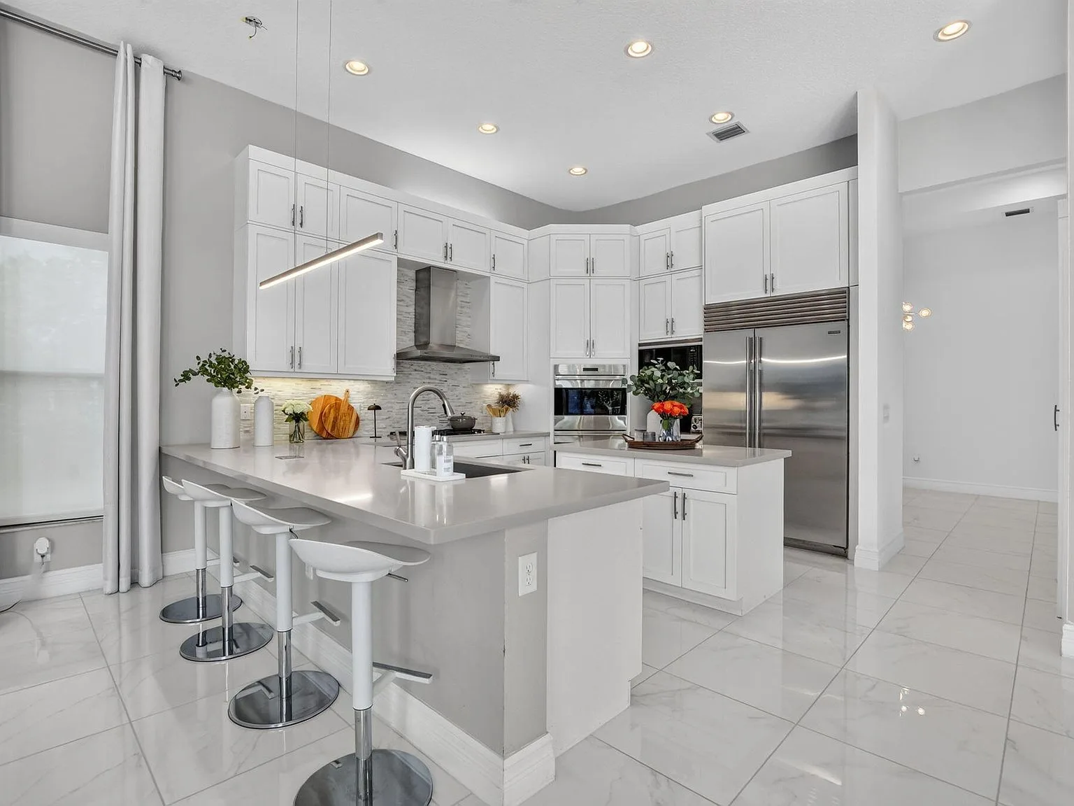 The renovated-style kitchen at 16740 Strasbourg Lane with stacked white cabinetry, quartz countertops, glass-tile backsplash and a breakfast island
