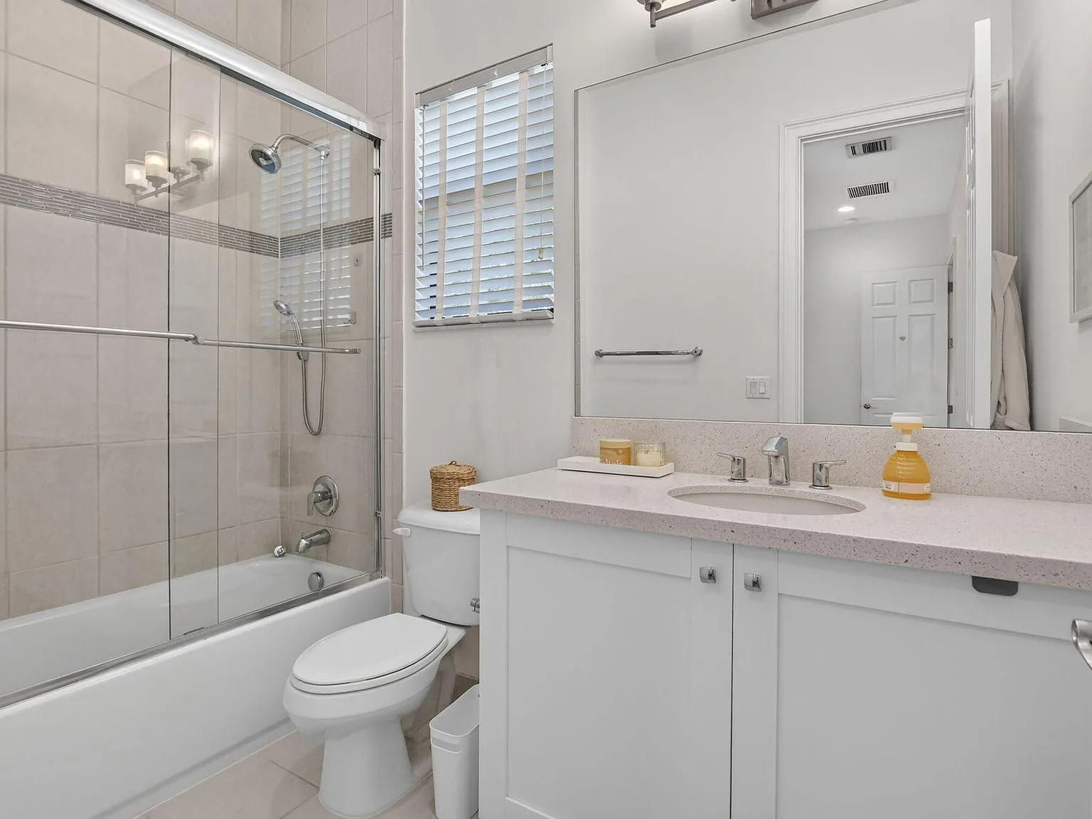 A bathroom vanity at 16740 Strasbourg Lane with quartz countertop, white cabinetry and a stone-tiled shower