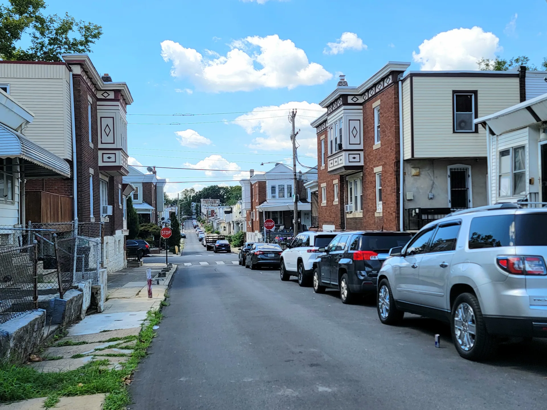 A residential street in Northeast Philadelphia lined with brick and siding homes under a clear blue sky