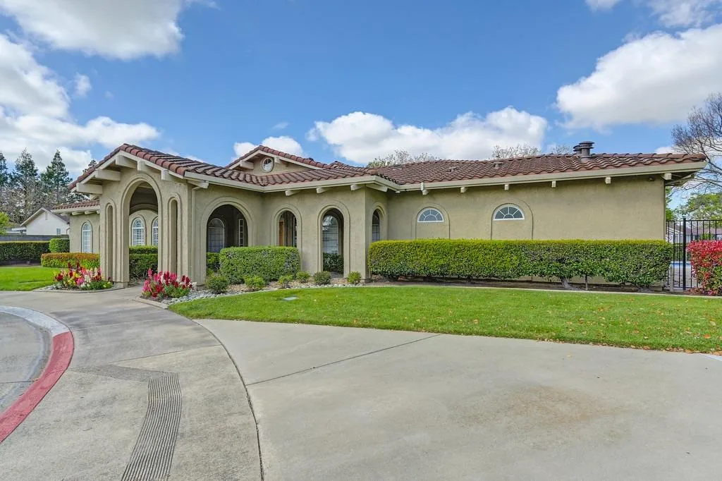 A Mediterranean-style single-story home with stucco walls, arched entry, and manicured front landscaping in a Northern California community