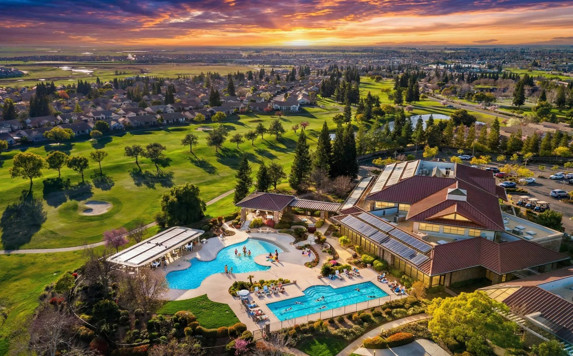 Aerial view of a 55+ resort community with clubhouse and pool at sunset