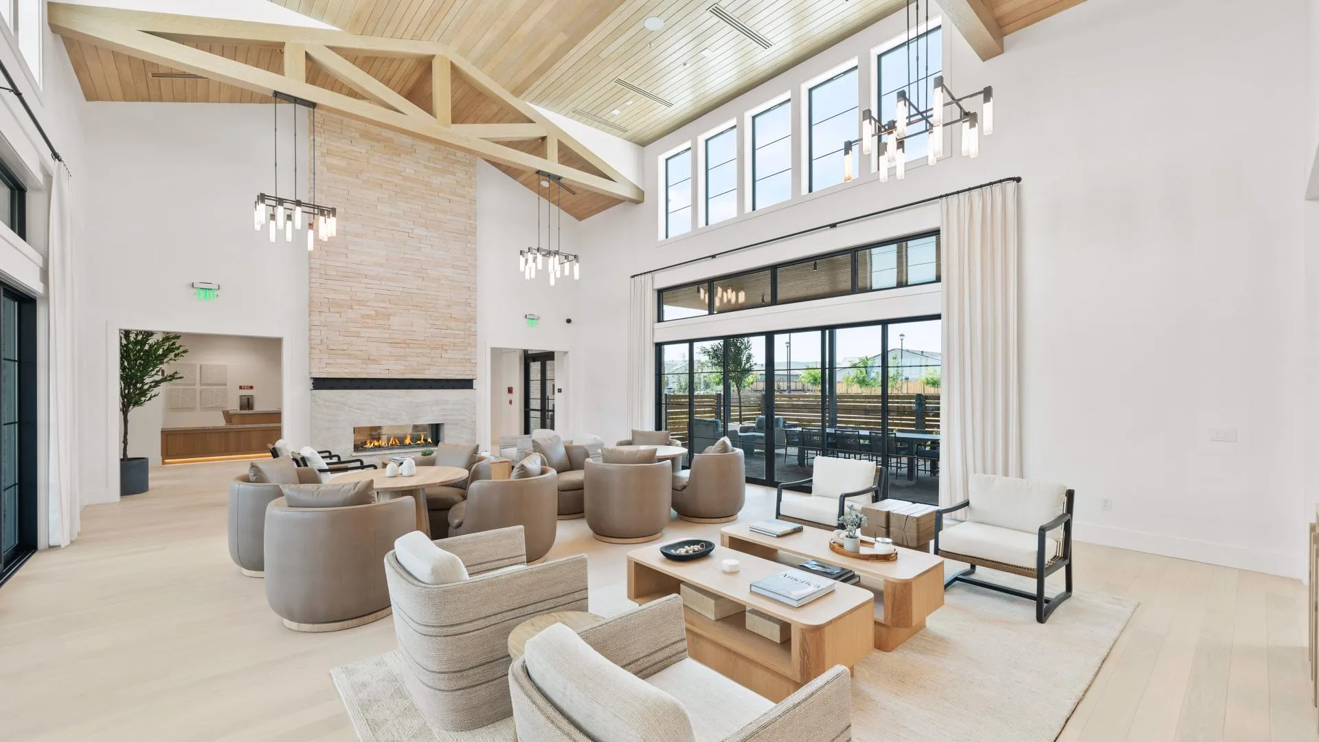 An open-concept great room in a modern single-story home with vaulted ceiling, stone fireplace, and light hardwood floors