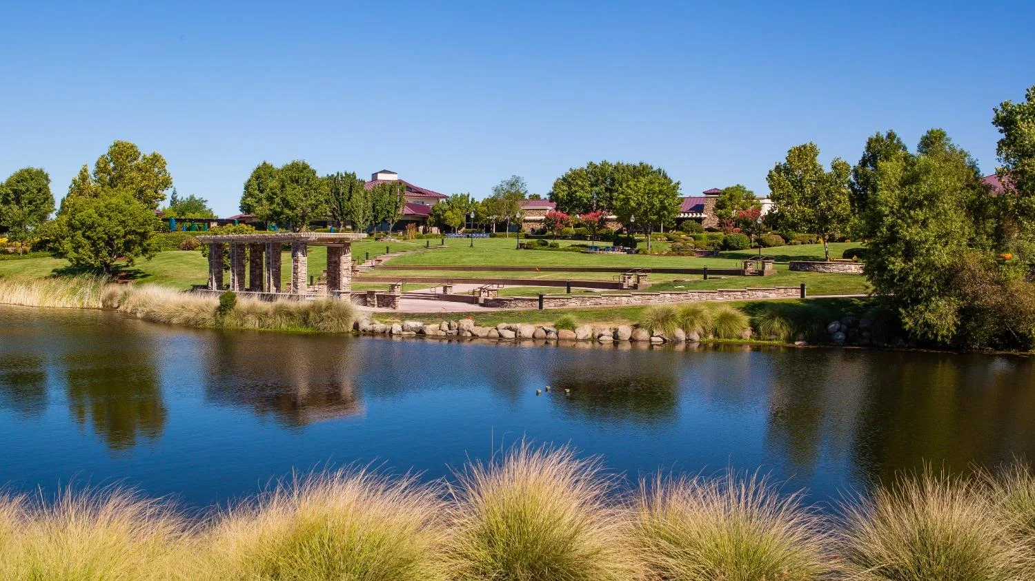 A calm landscaped park with a stone pergola beside a lake at a Northern California community