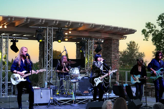 An outdoor community performance at dusk in a Northern California 55+ community, with a band on a stone pavilion stage.