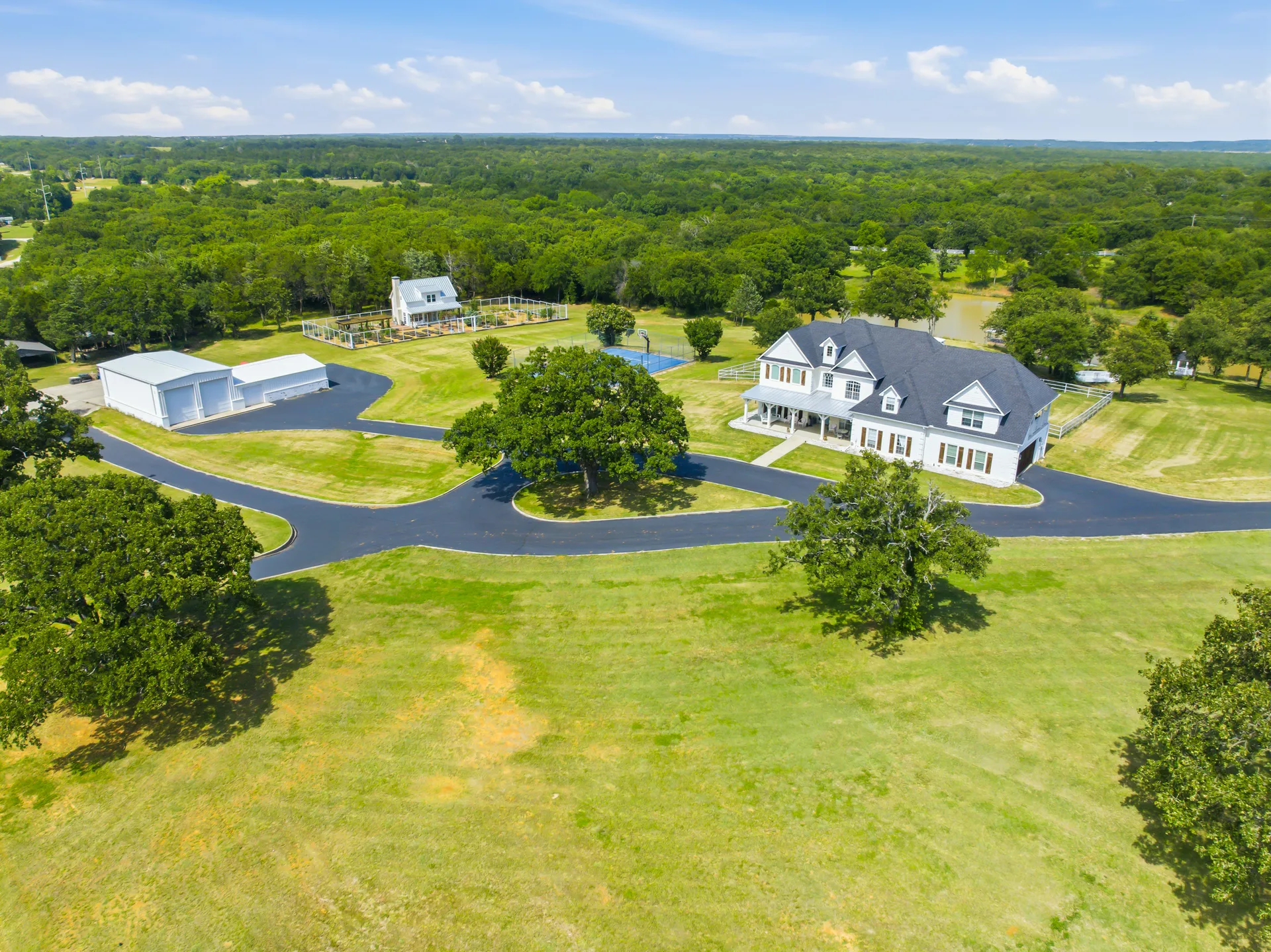 Aerial view of a North Texas farmhouse estate with its workshop and basketball court on a bright day