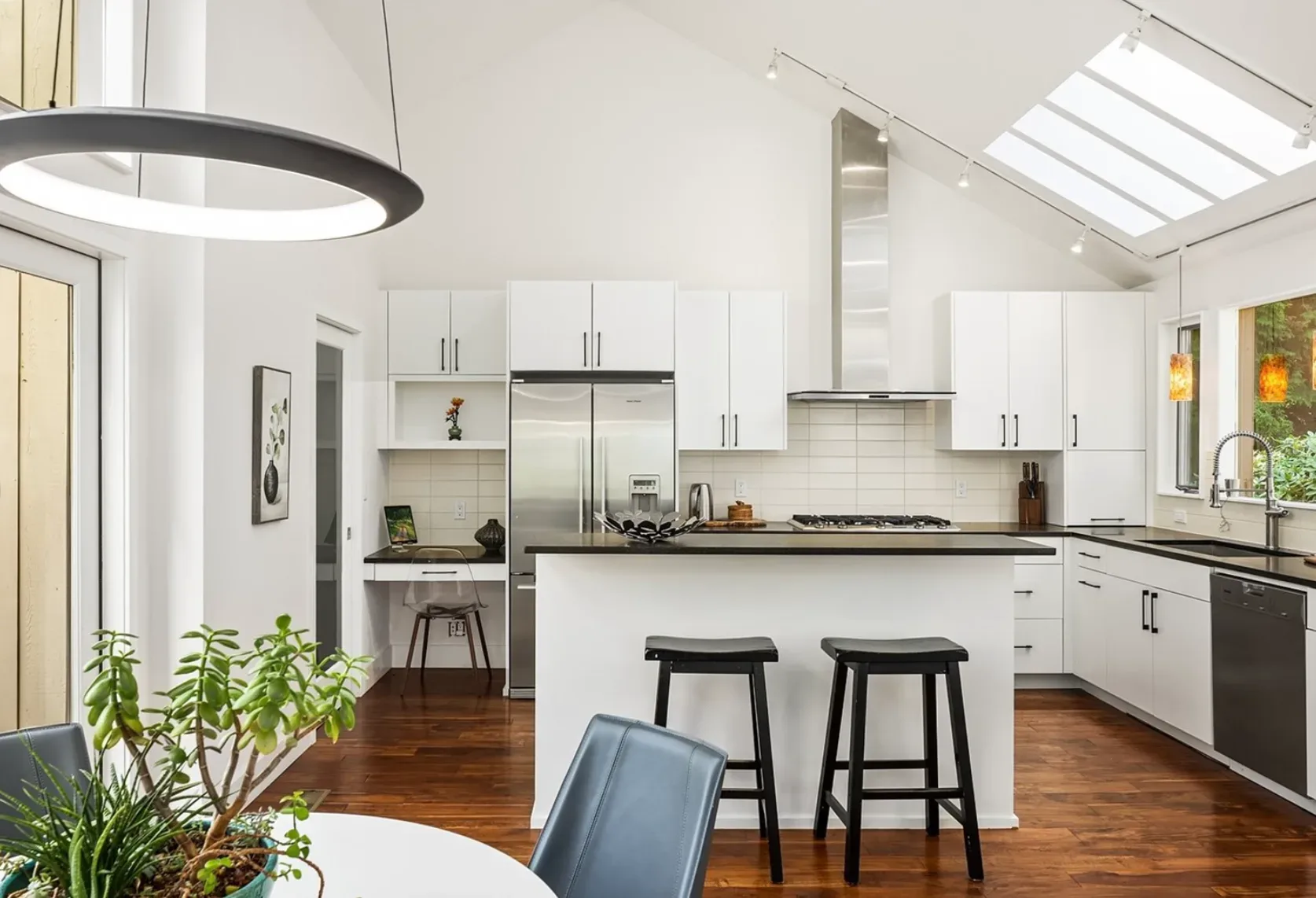 Kitchen with a vaulted ceiling and skylights, white cabinetry, and dark counters that opens to the living and dining spaces