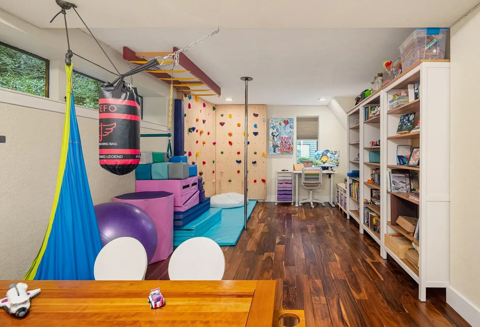 Playroom with a climbing wall, monkey bars, a hanging punching bag, and built-in shelves with a desk nook