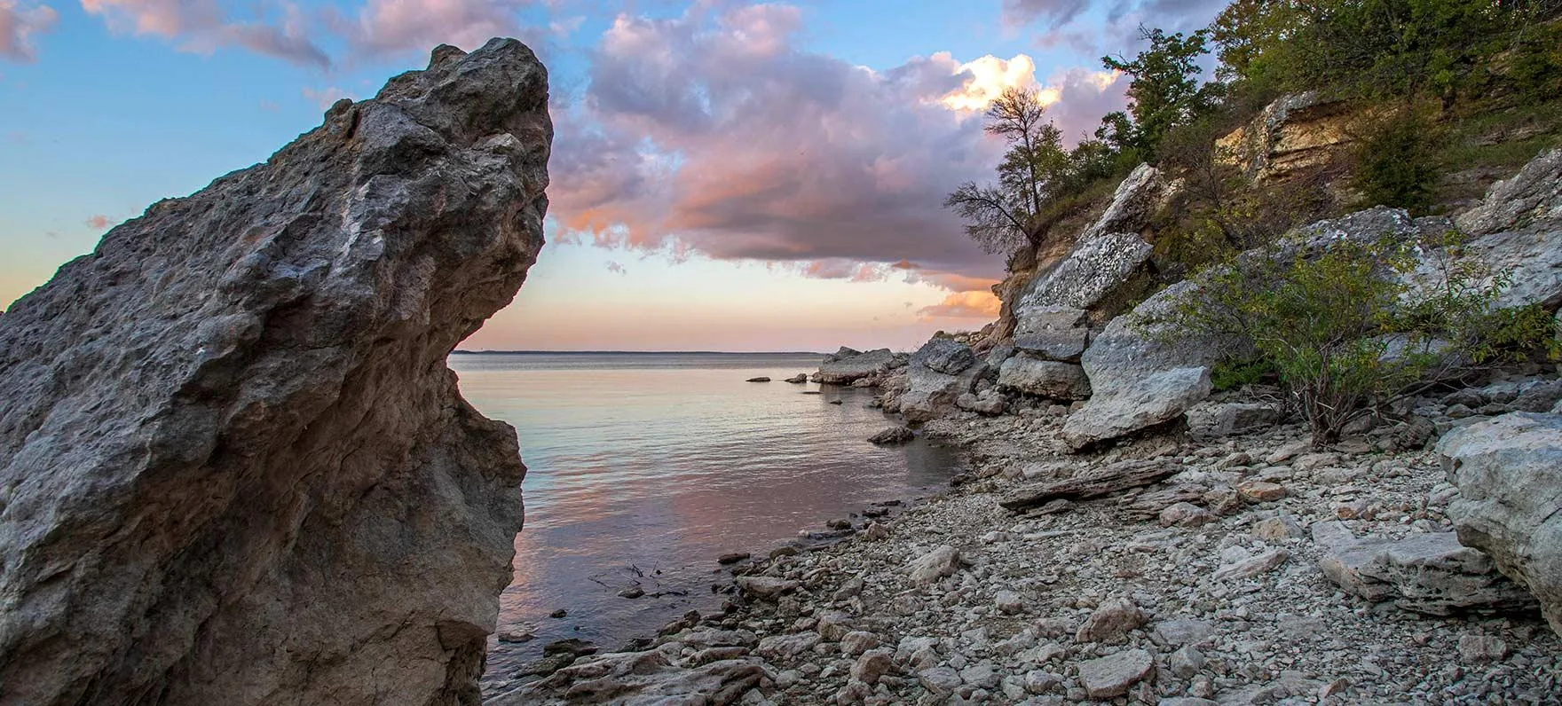Rocky shoreline of Lake Texoma glowing in pink and gold sunset light