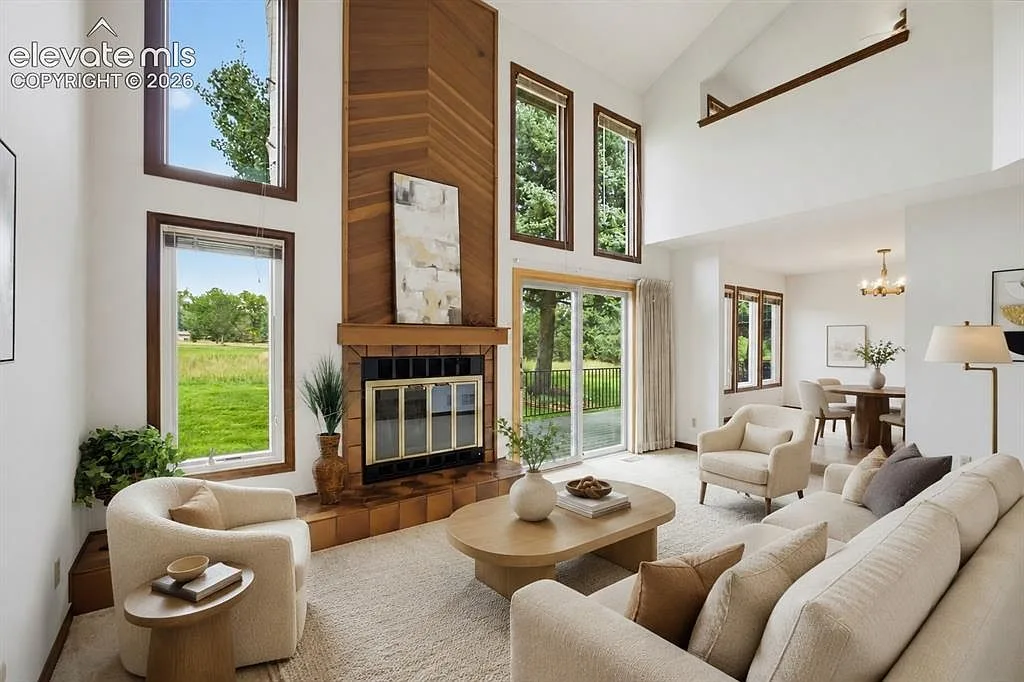 Vaulted living room with floor-to-ceiling windows and a wood-paneled fireplace