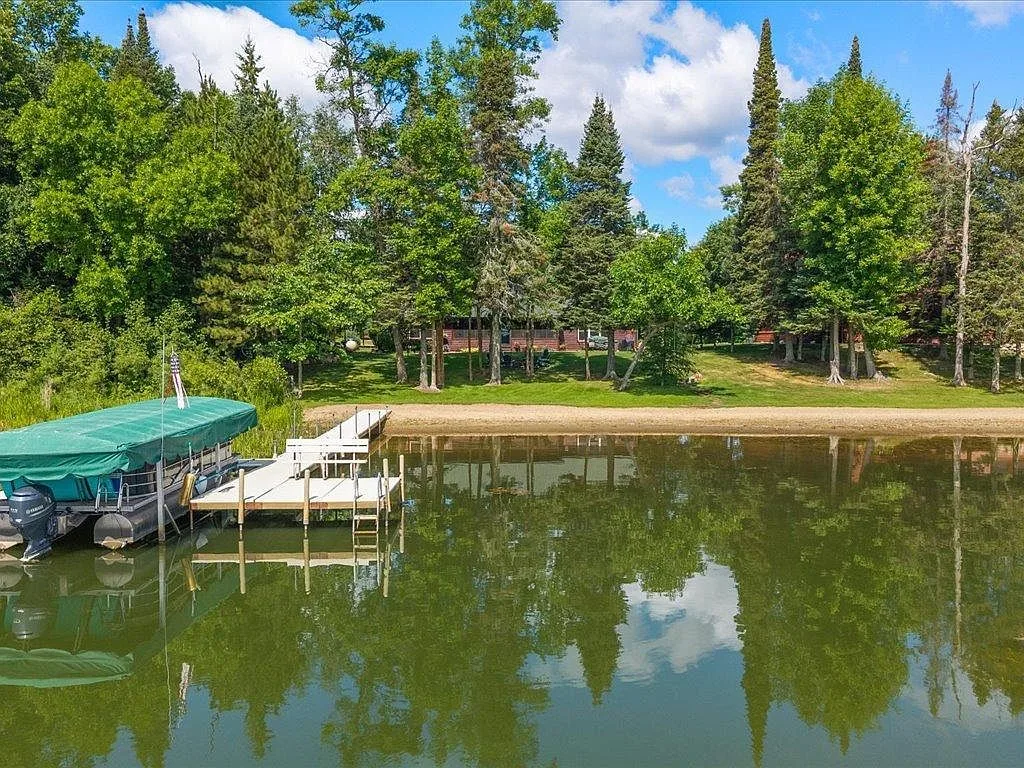Water-level aerial looking toward the sandy beach, dock, and lake home