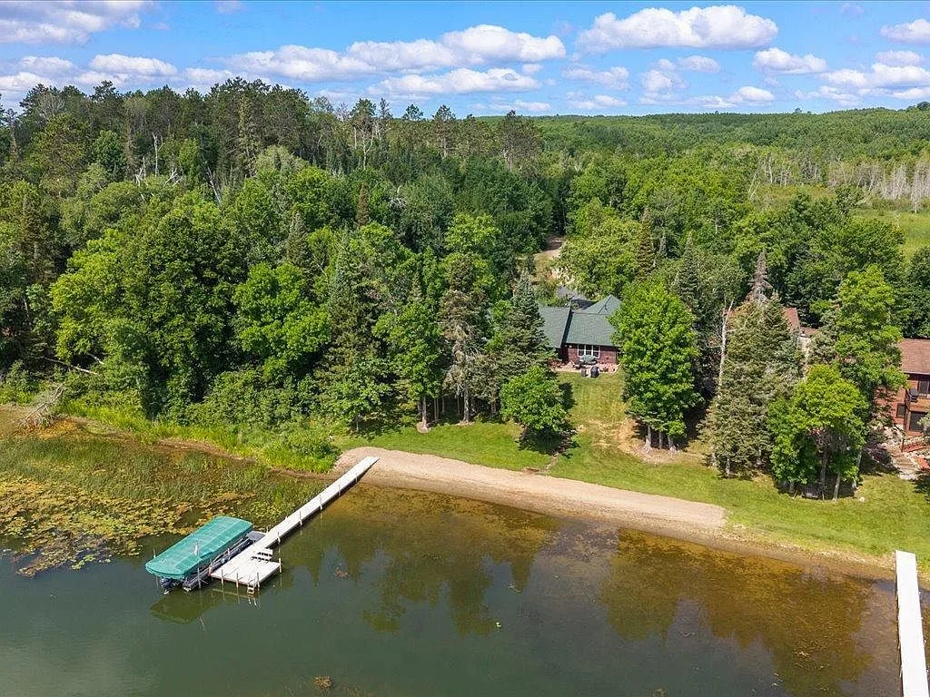 Aerial view over Mitchell Lake toward the sandy beach, dock, and wooded property at 16138 Zigmund Dr