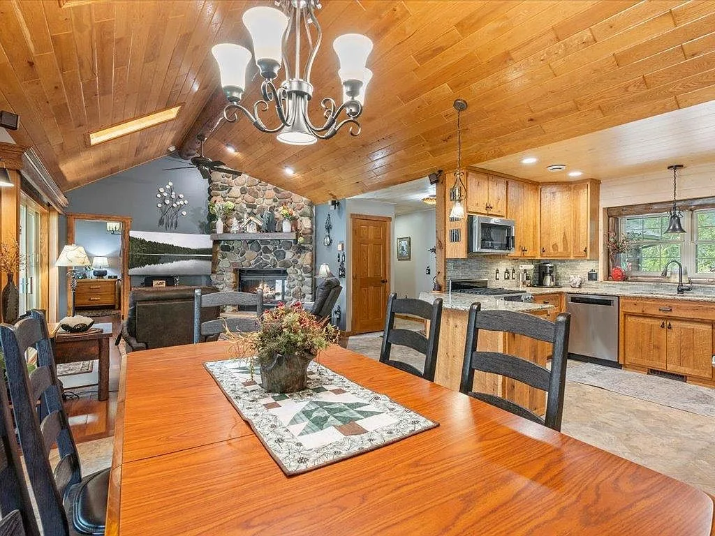 Open dining and kitchen at 16138 Zigmund Dr with vaulted wood ceiling, fieldstone fireplace, and lakeside windows