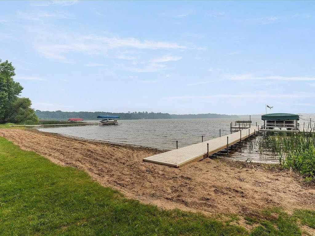 Private sandy beach with a long wooden dock, boat lift, and level lawn at Mitchell Lake
