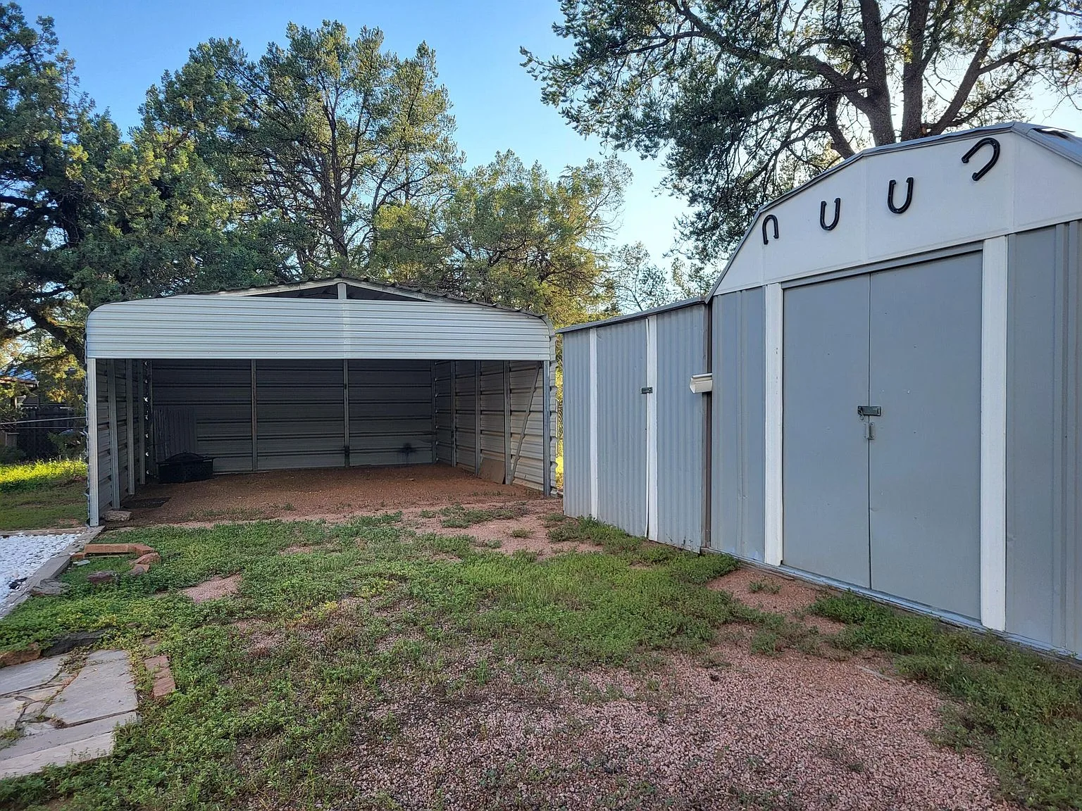 Fenced back yard at 510 E Evergreen St with a metal carport and two large storage sheds