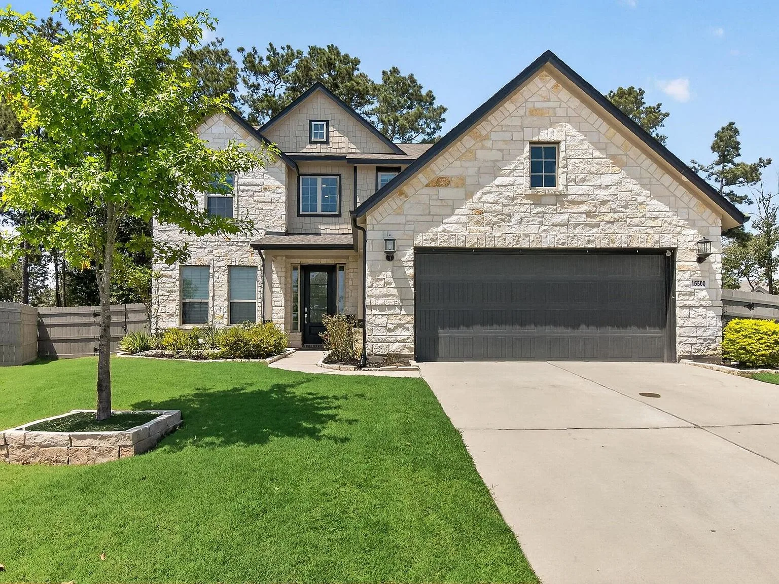 Front exterior of the two-story stone and siding home at 15500 Leopard Lily Ln, with a manicured lawn under a clear blue sky