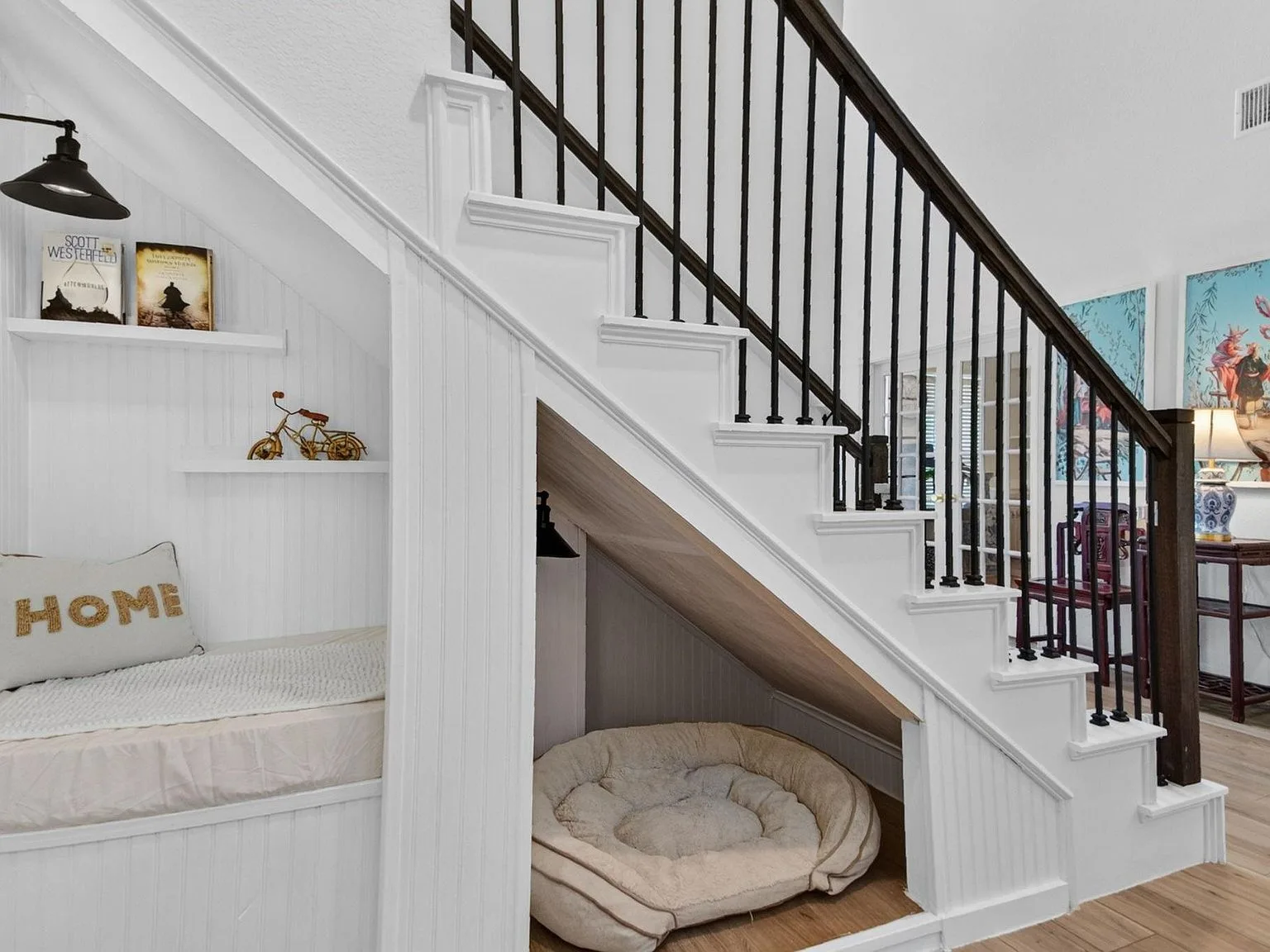 Reading nook and pet nook tucked under the stairs with bookshelves and black iron railing