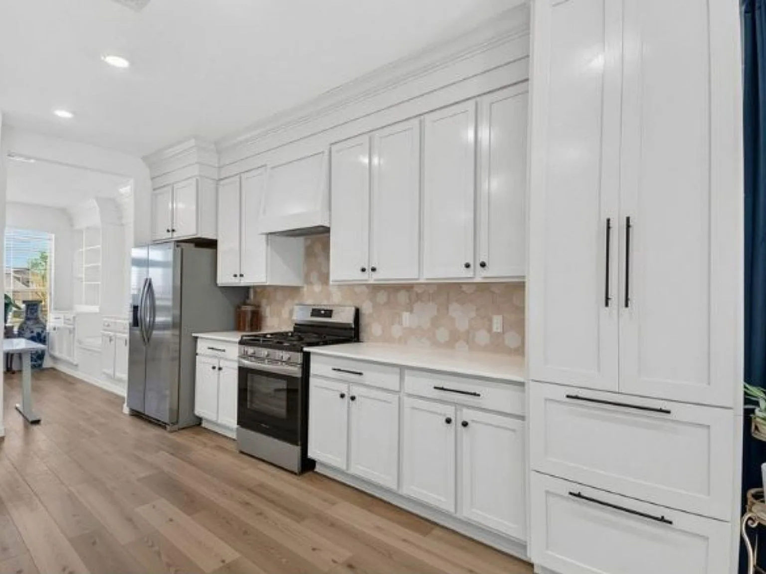White kitchen with shaker cabinets, hexagon tile backsplash, and stainless steel appliances