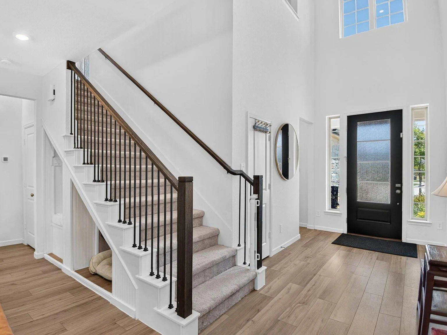 High-ceilinged entry foyer with wood flooring, carpeted stairs, and black metal railings