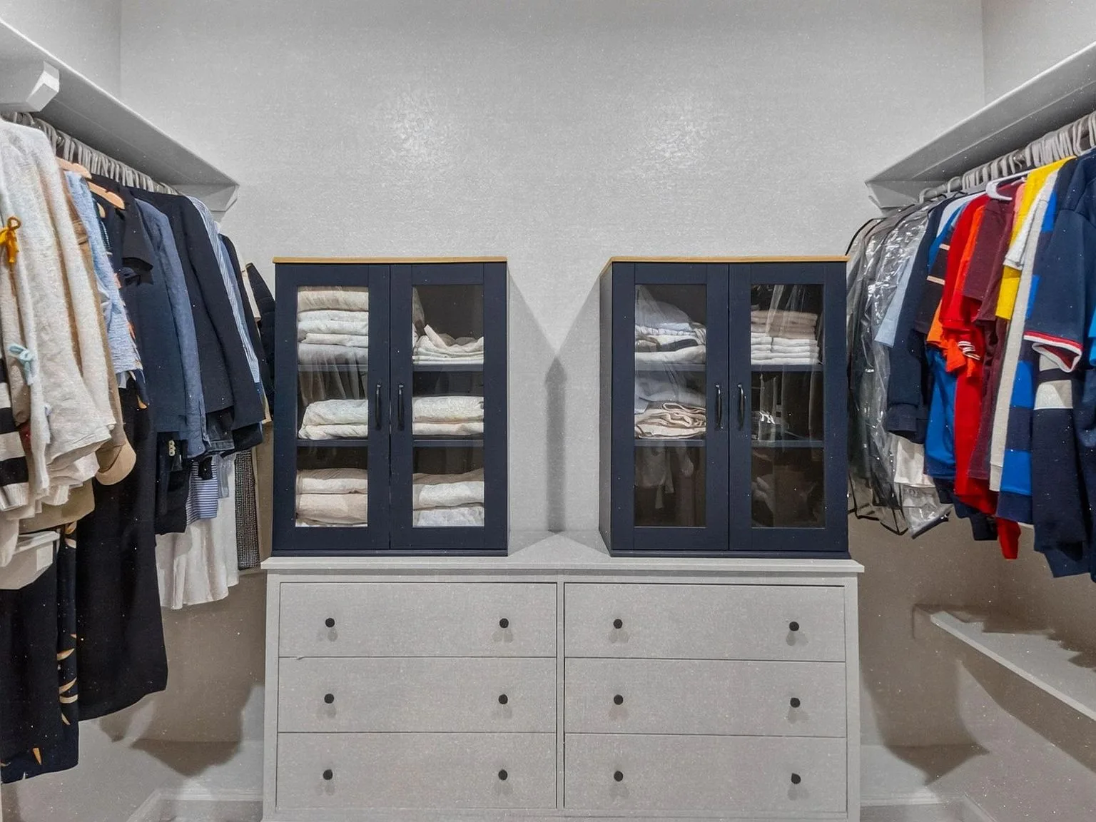 Walk-in primary closet with white and navy custom millwork, glass doors, and shelving