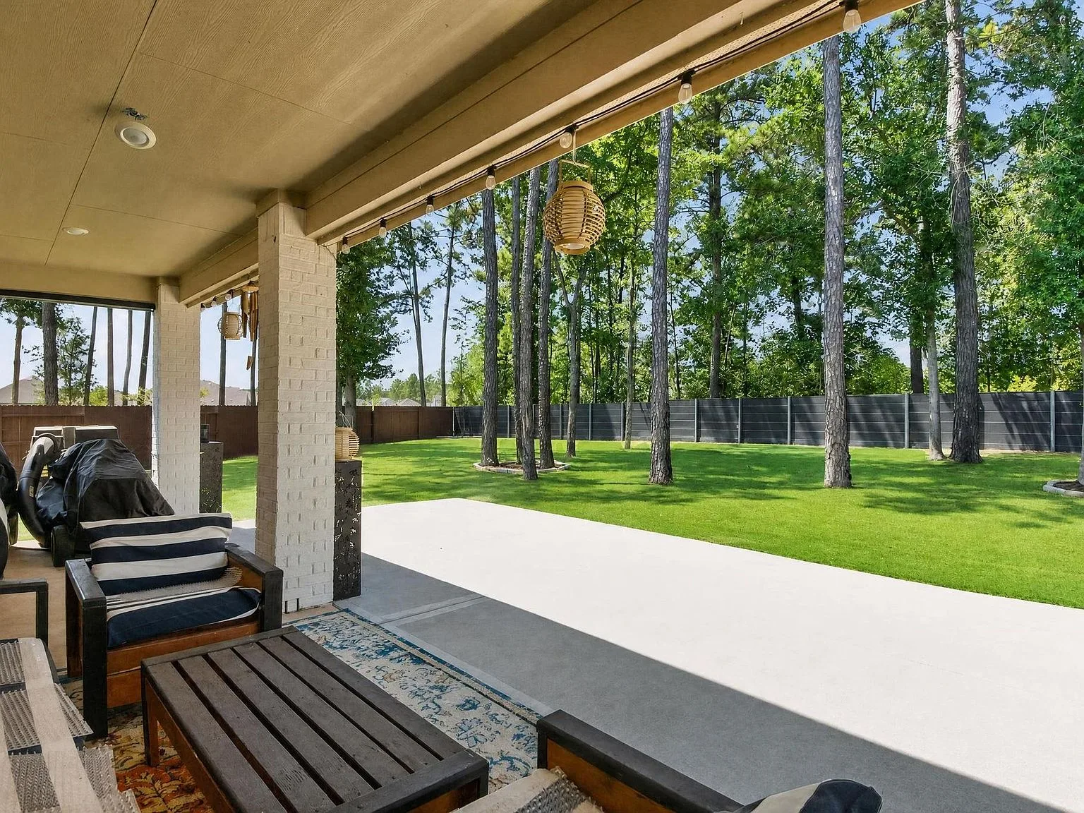 Covered patio with a white brick pillar, lounge seating, and string lights looking over the lawn