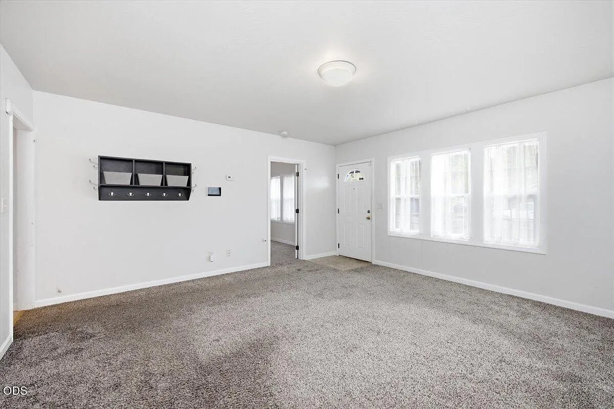 Bright living room with neutral walls, gray carpet, and natural daylight