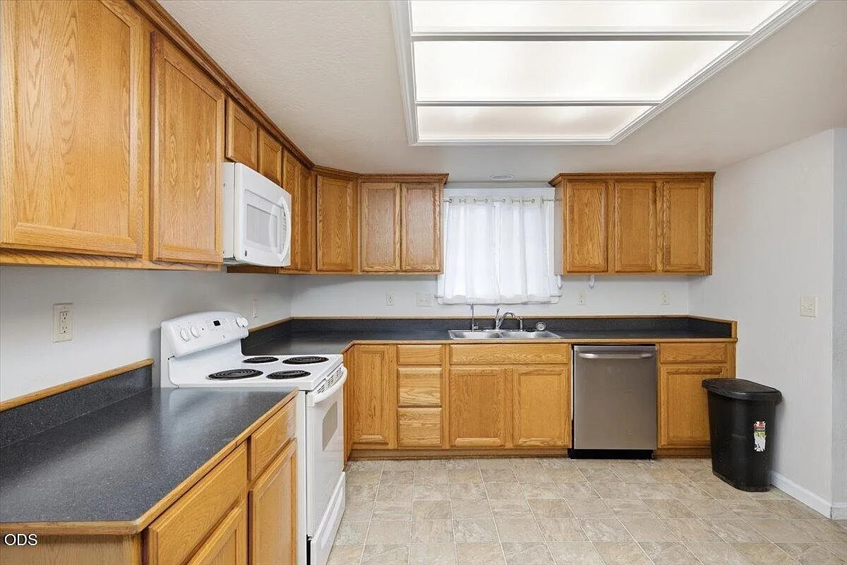 Kitchen with honey oak cabinetry, dark laminate counters, and white appliances