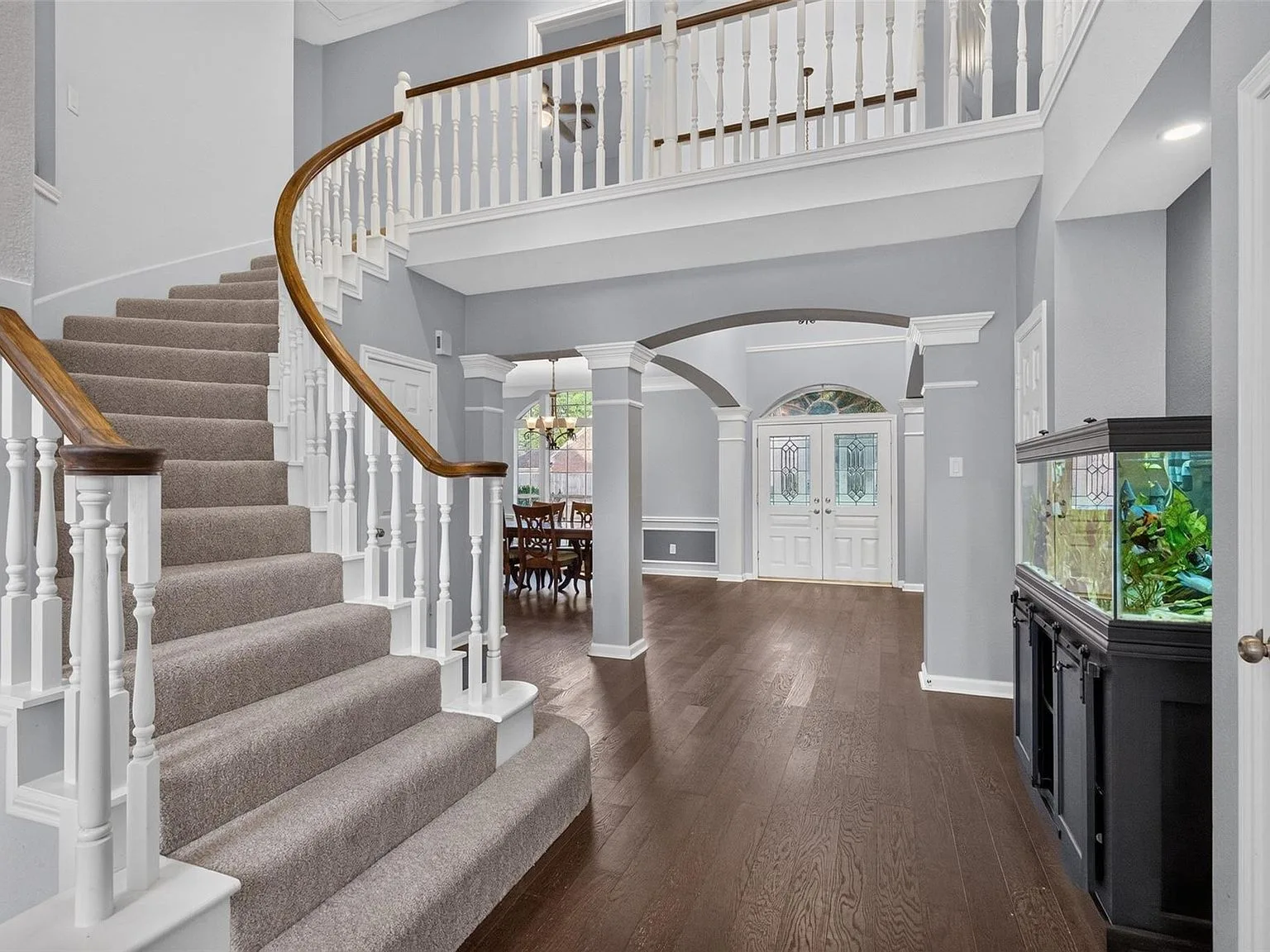 Grand foyer with a curved staircase, arched columns, and hardwood floors