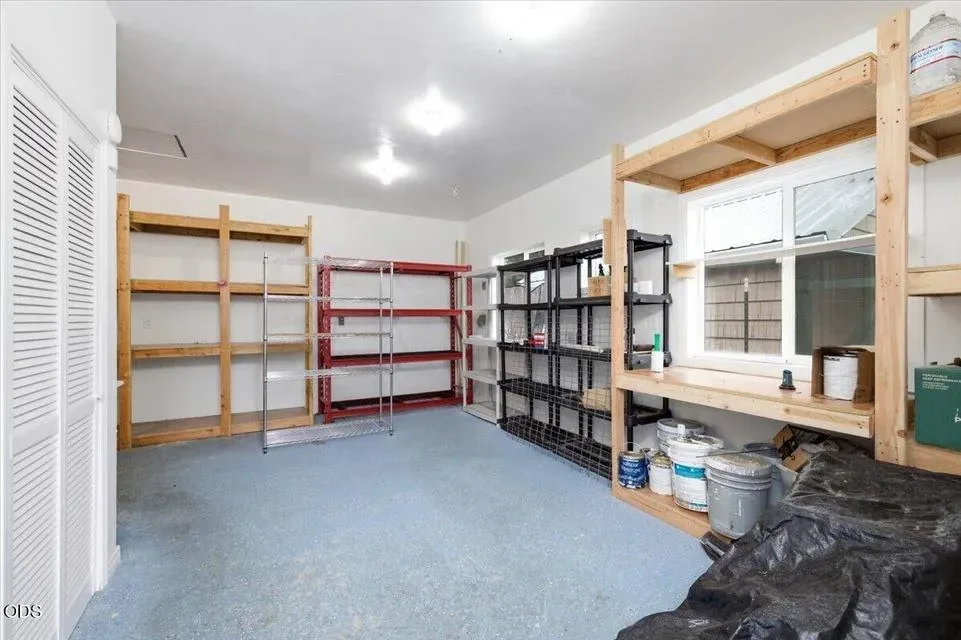 Interior of the detached storage and workshop building with a light blue painted concrete floor, white walls, and heavy shelving