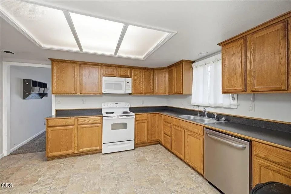 Bright kitchen with honey oak cabinetry, a window over the sink, and white appliances
