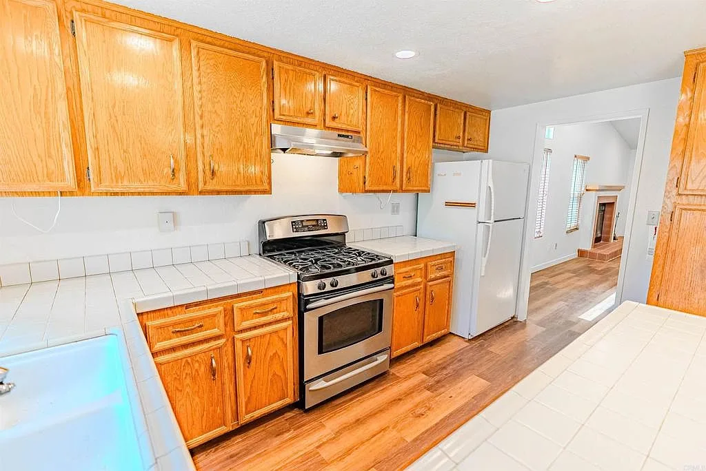 Kitchen with oak cabinetry and tile counters looking to the living room