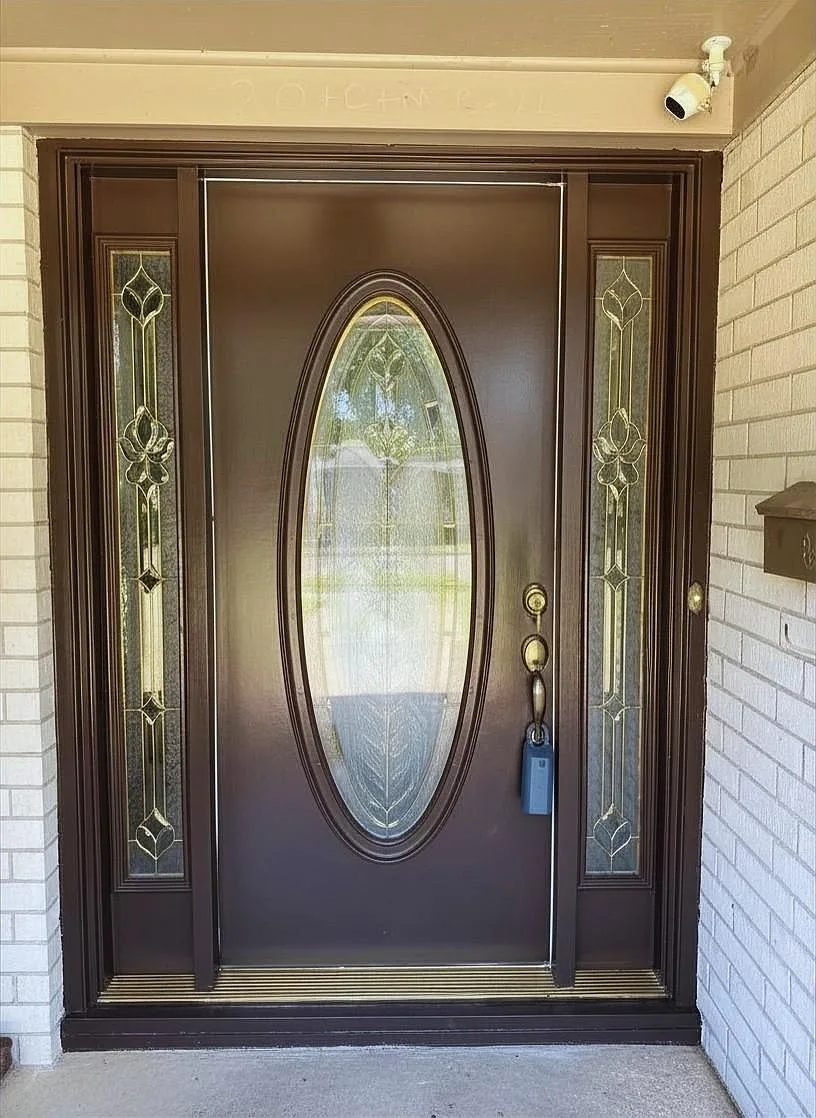 Front door with an oval leaded-glass insert and white brick siding