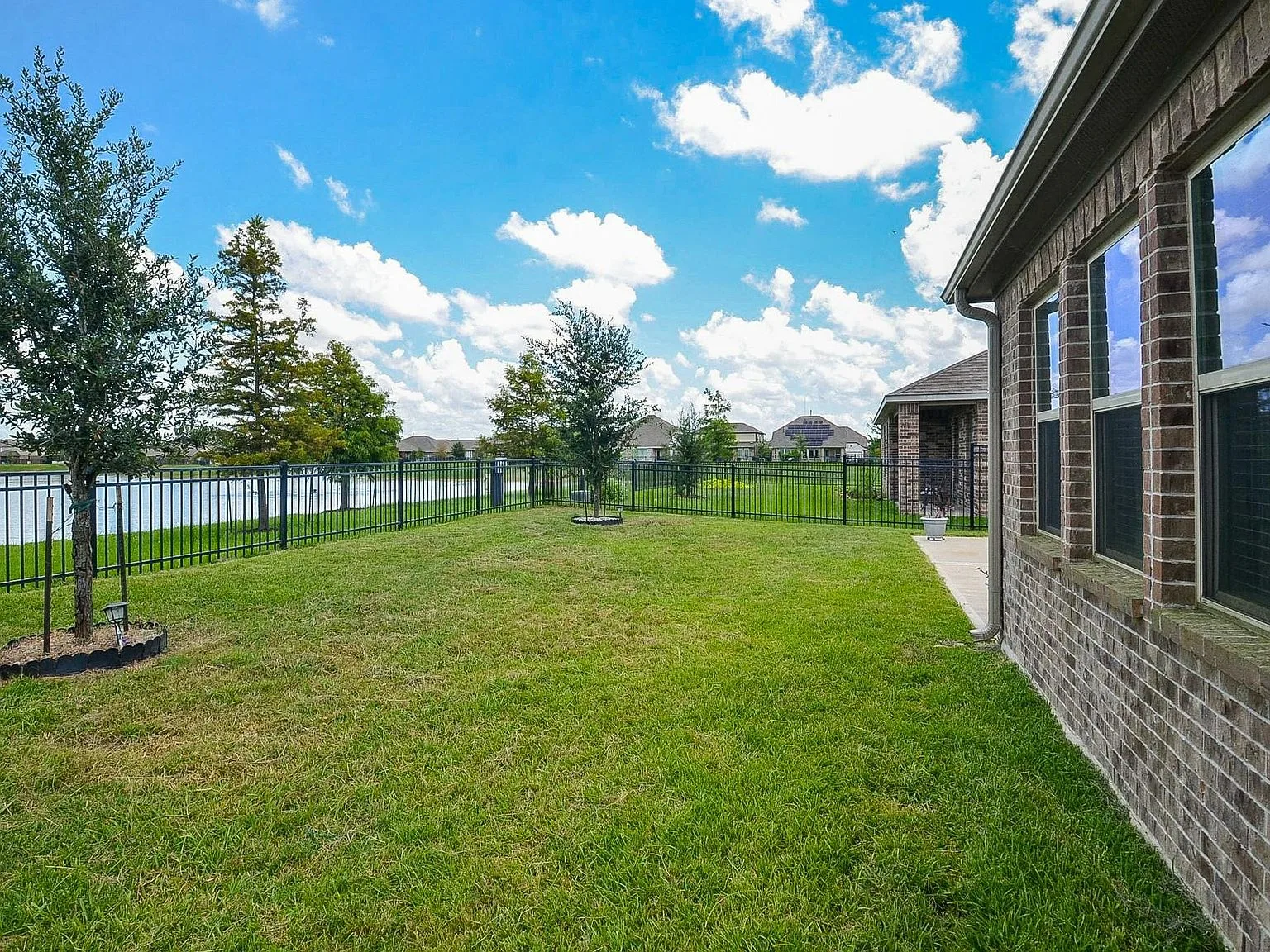 Manicured backyard with black metal fencing beside the community lake