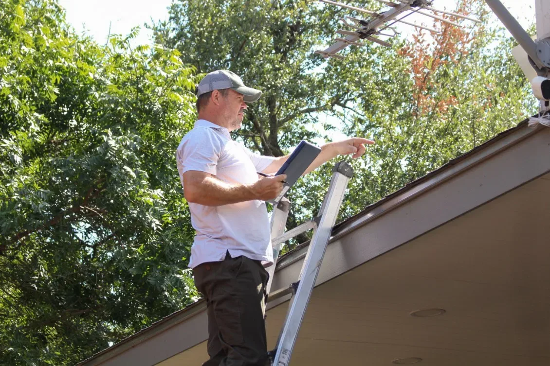 A Rodeo Home Inspections LLC inspector on a ladder pointing out roofline details during a pre-listing inspection