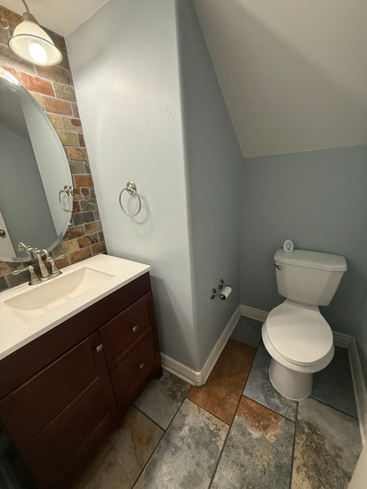 Powder room with stone accent wall, oval mirror, and quartz vanity