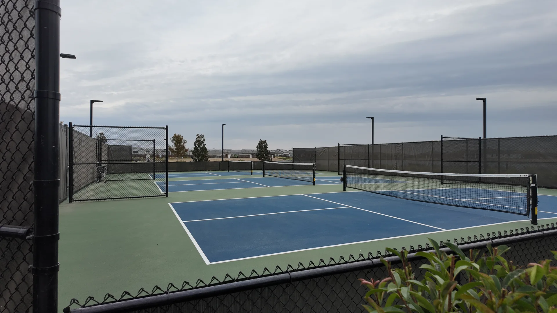 Fenced pickleball court complex at the Lakeview Club at Del Webb at River Islands in Lathrop, California, with permanent nets, windscreens and court lights