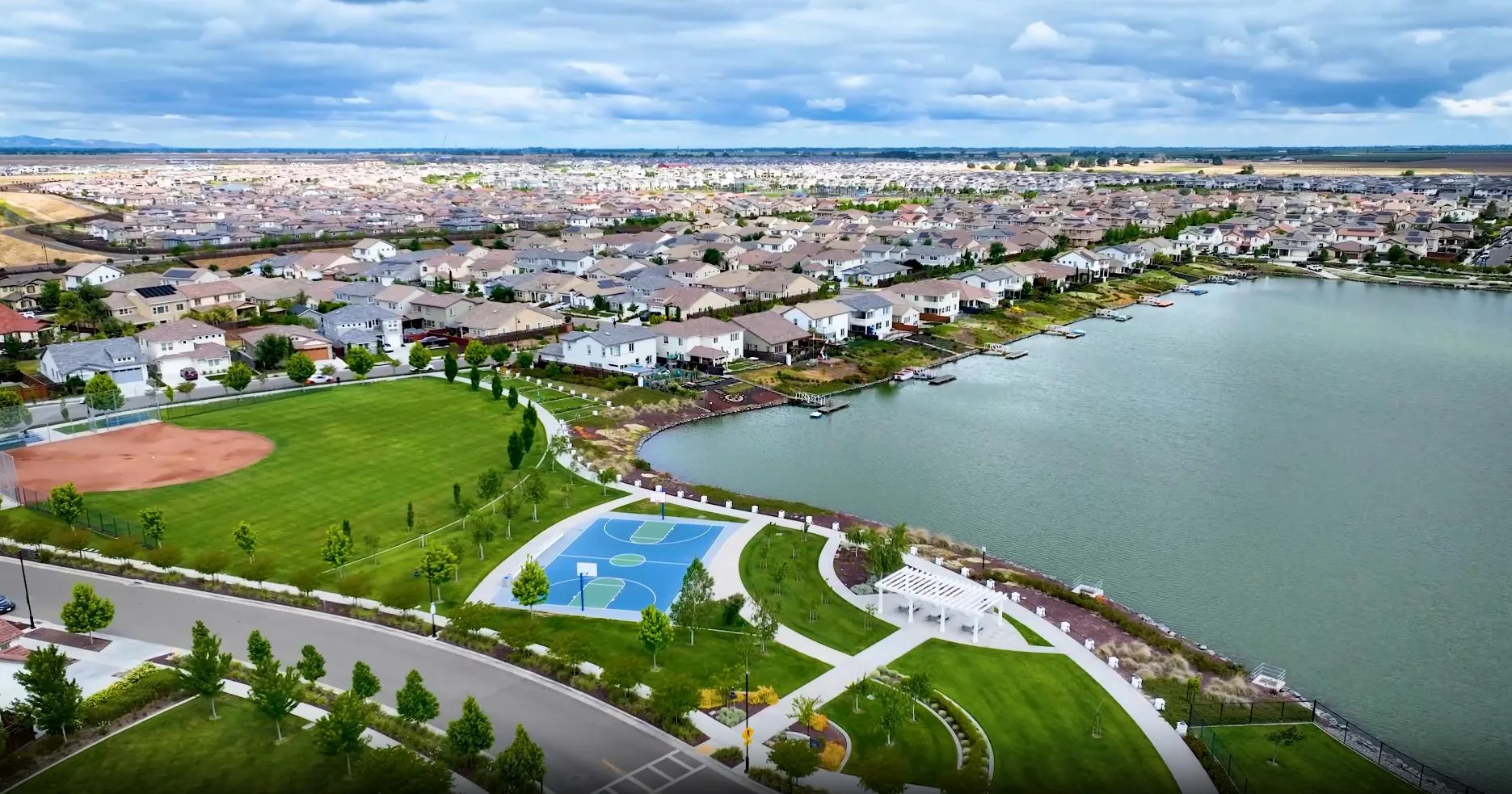 Aerial view of River Islands in Lathrop, California, in a single frame: homes, a lake, docks, a baseball field and a basketball court